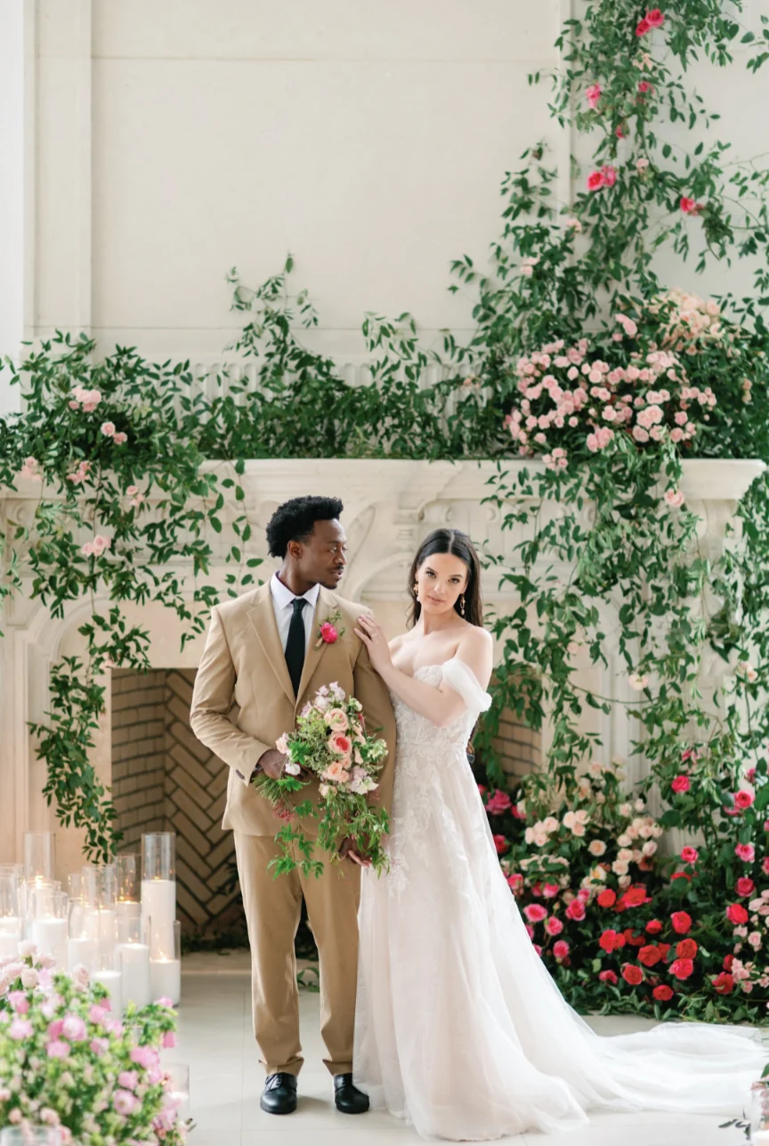 Couple beside a fireplace framed with trailing greenery and pink garden roses