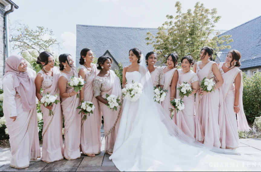 Bride with her bridal party in blush saris and gowns, each holding a white bouquet